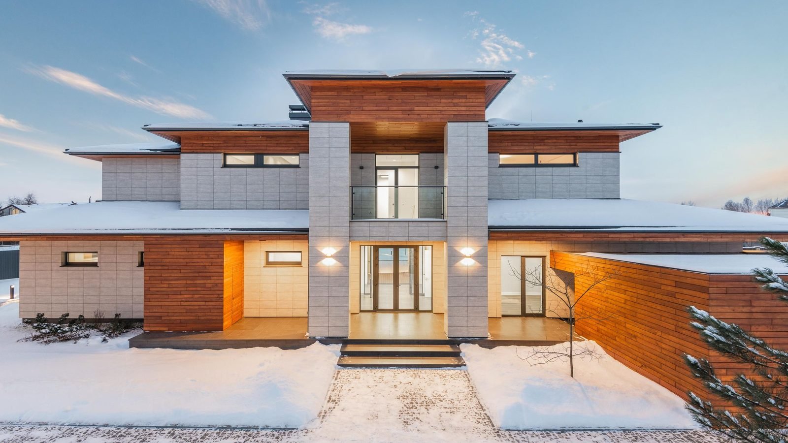 Modern house under snow with full-height glazing and lit entrance doors