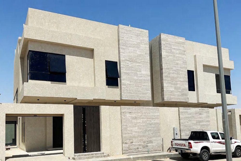 A stone-clad villa in Dammam with an exposed-frame curtain wall and dark-framed glazing above a paved forecourt