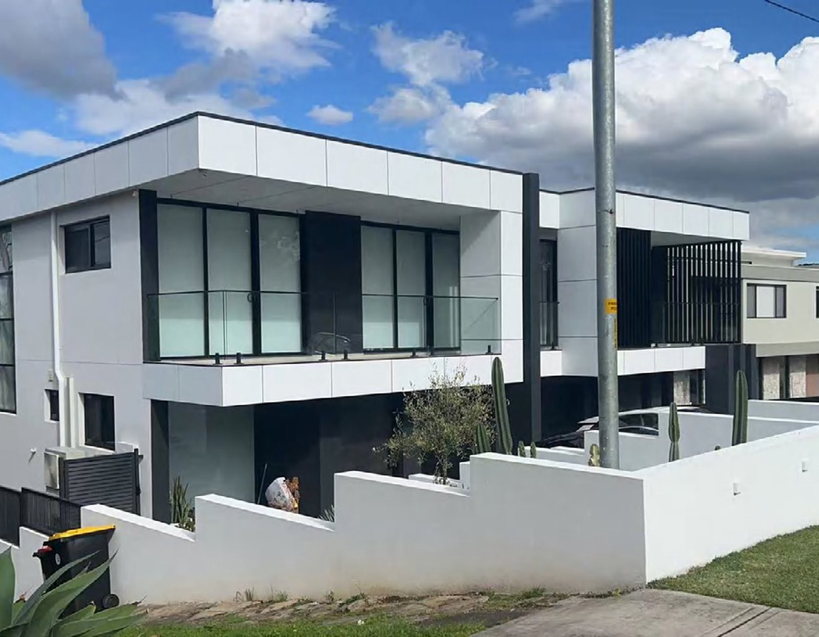 A modern Australian house with a double-height glazed frontage, a rendered facade and a landscaped lawn