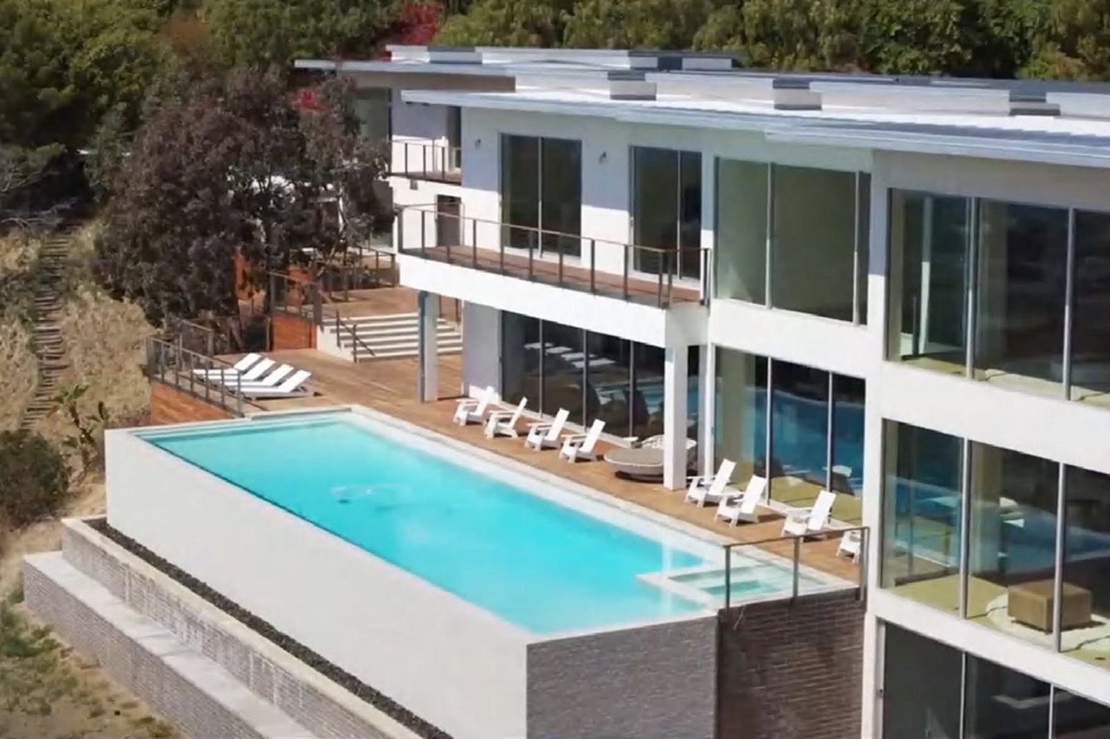 A white American villa with a pool terrace and a fully glazed rear wall opening to the garden