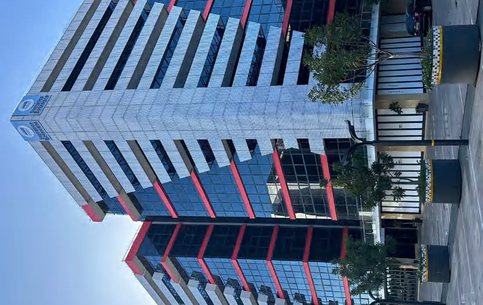 A Lagos building wrapped in a fully glazed curtain wall reflecting the sky, framed by stone-clad piers