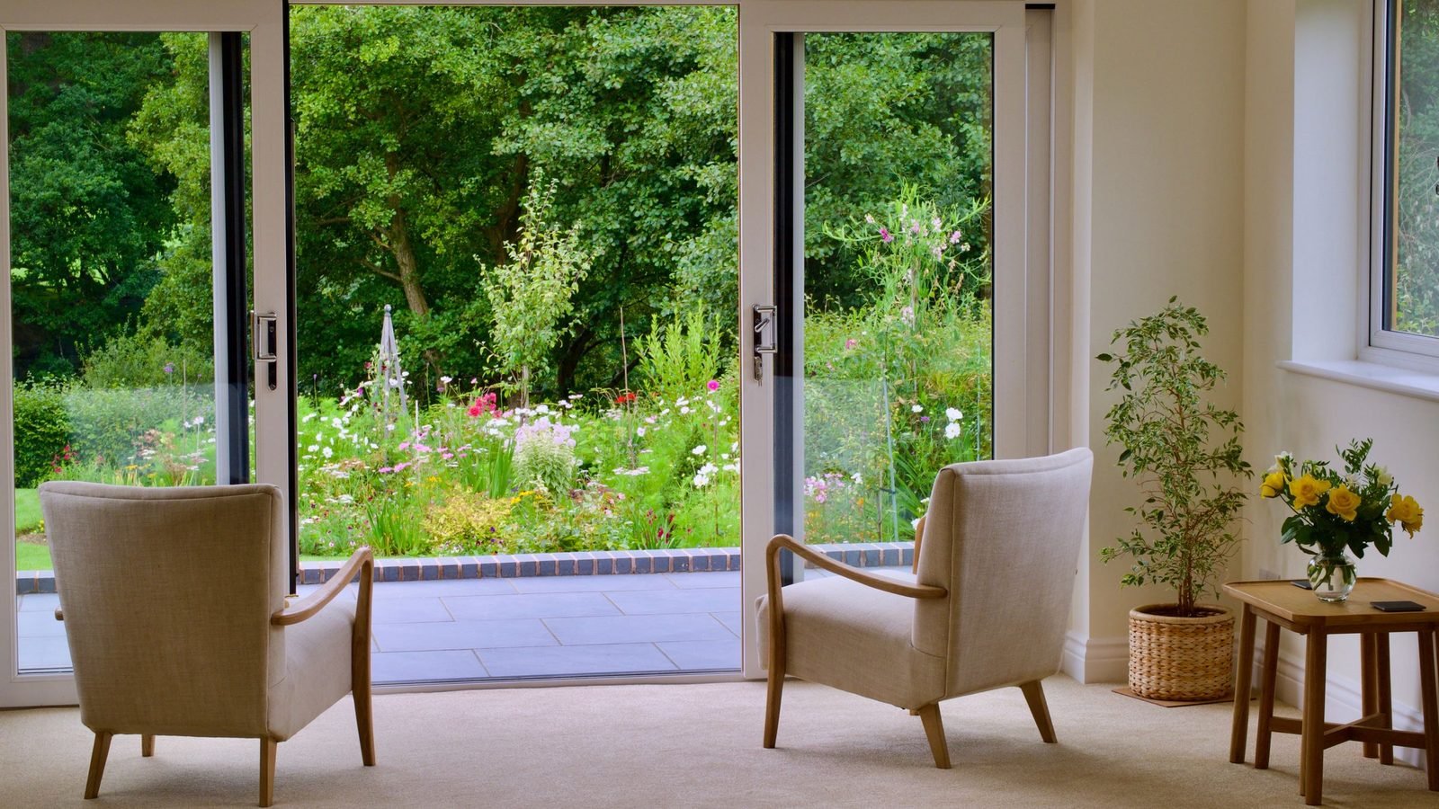 Pair of slim-frame glazed doors seen from inside a room, both leaves open onto a garden