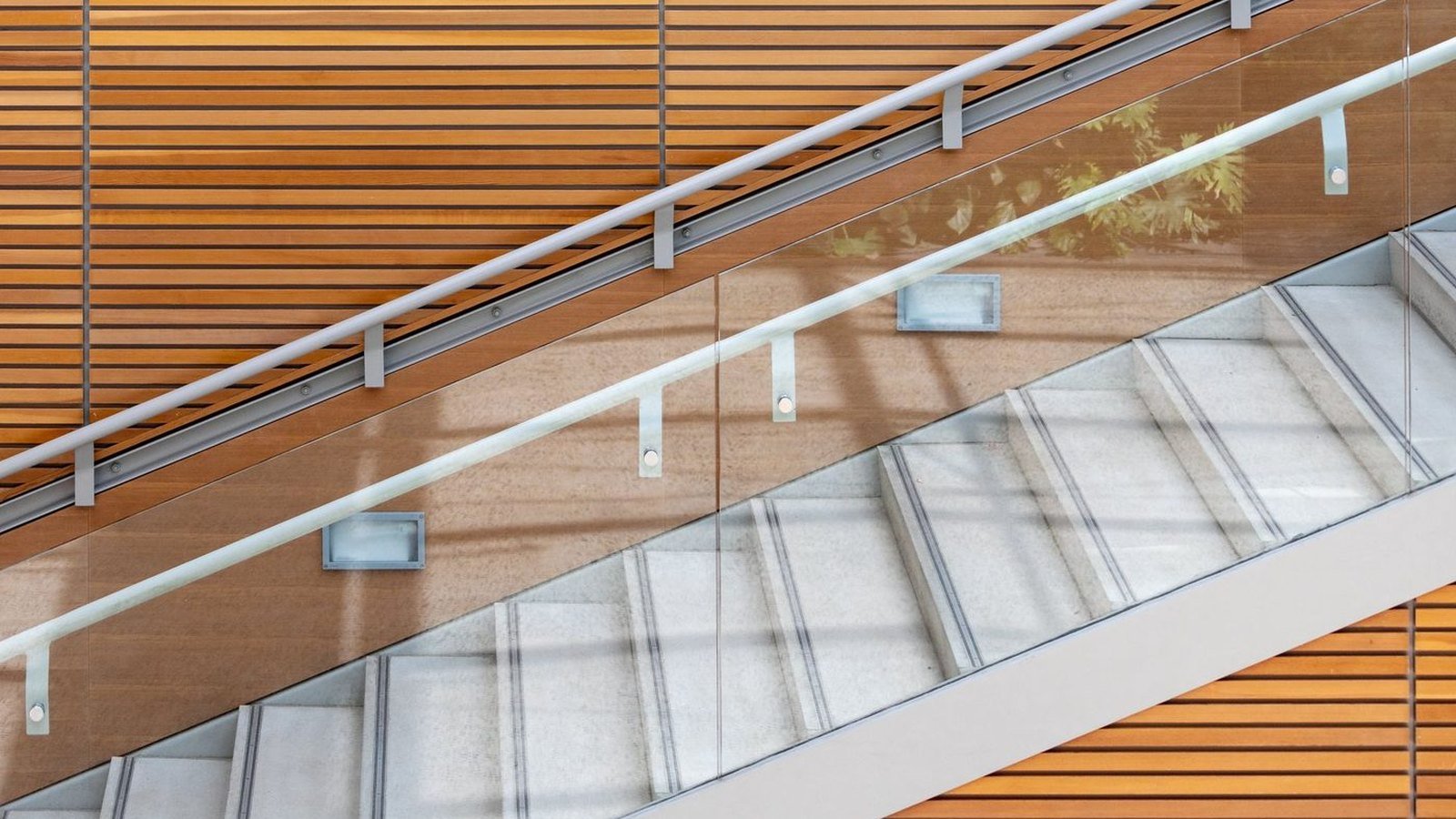A glass balustrade along a concrete stair, the handrail carried on brackets above the glass