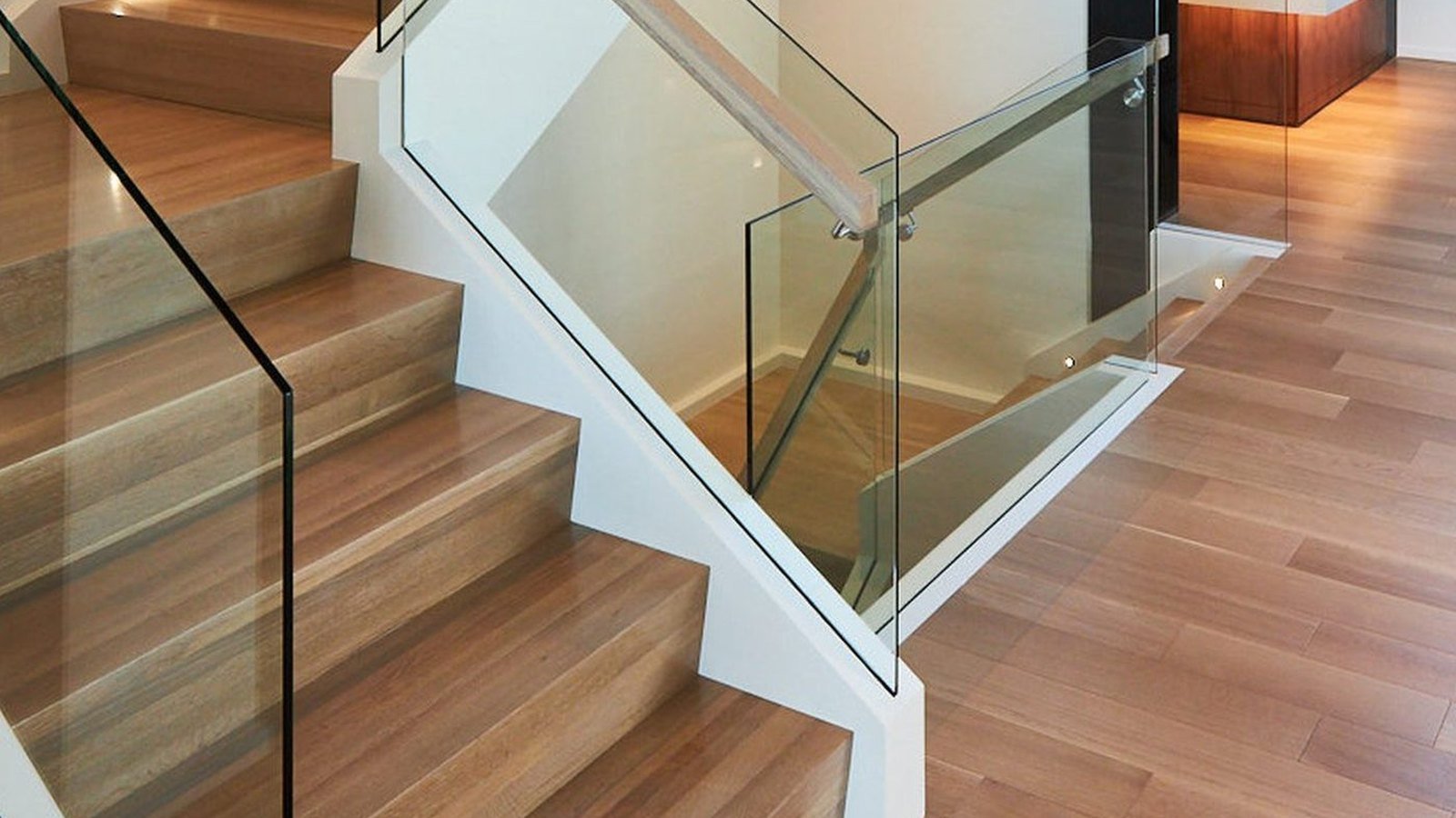 A frameless glass balustrade beside a timber staircase, the panel set into a floor channel beside a slim handrail