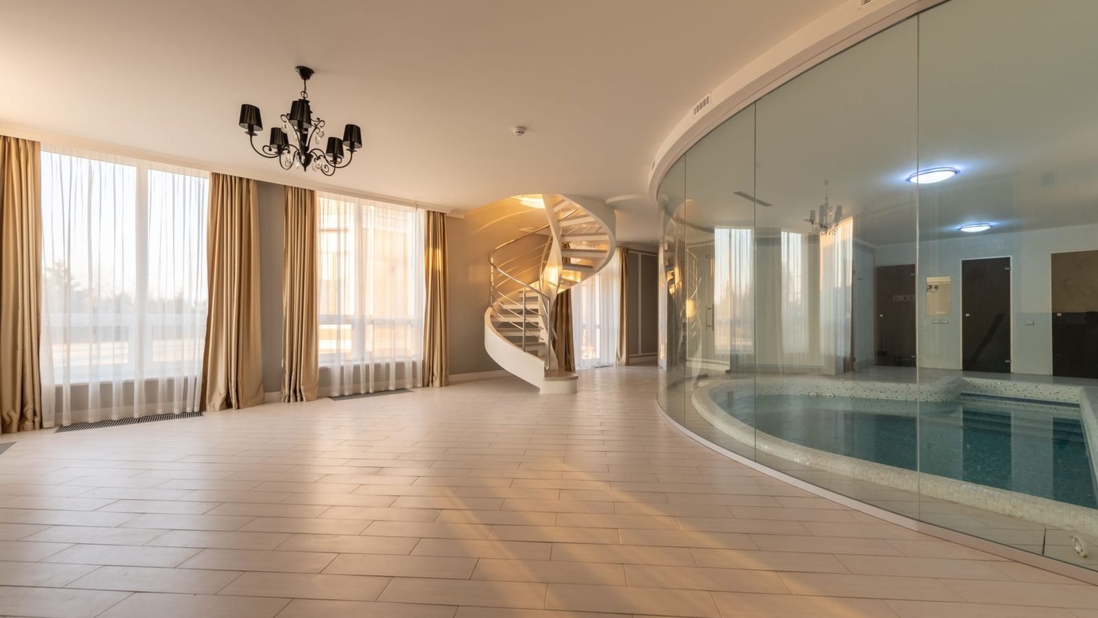 A curved glass wall enclosing an indoor pool, seen from a tiled hall