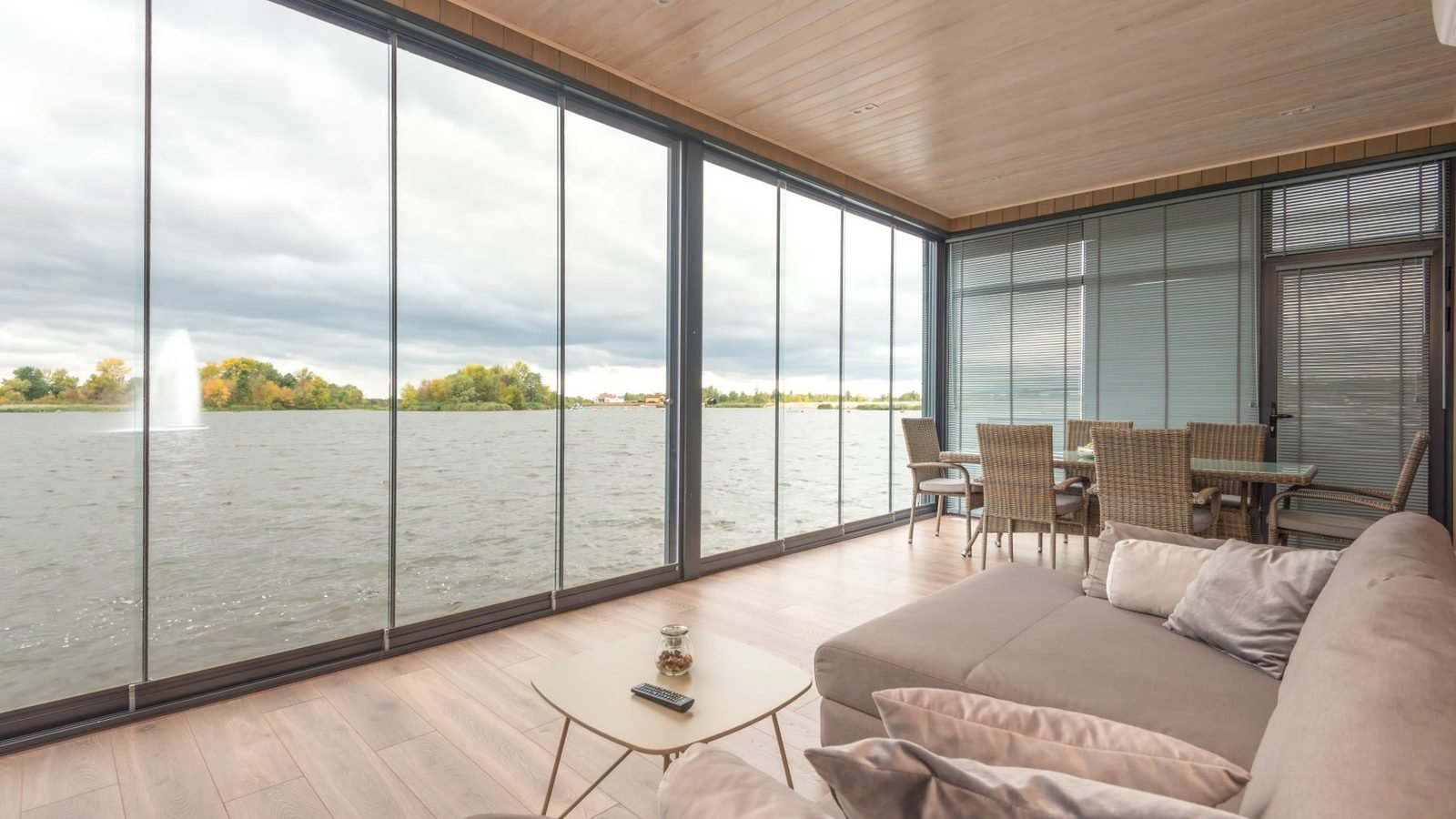 A living room glazed end to end, the glass wall turning a corner without a post, a lake beyond