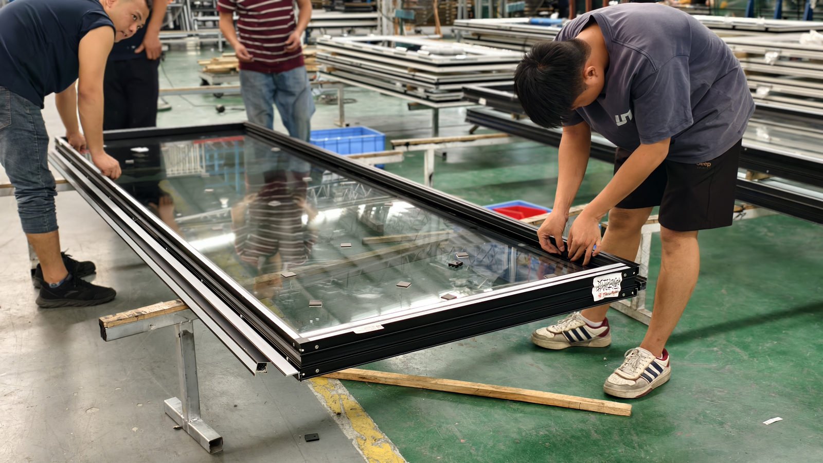 Two workers lowering an insulated glass unit into an aluminium sash