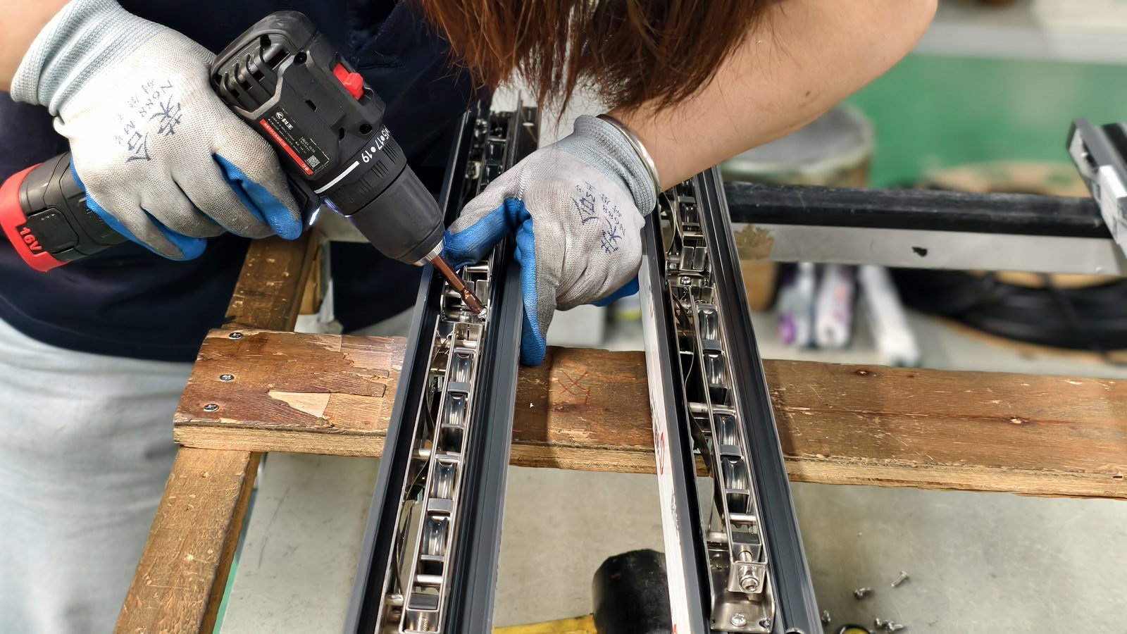 Worker's gloved hands fitting a corner bracket and hardware into an aluminium profile