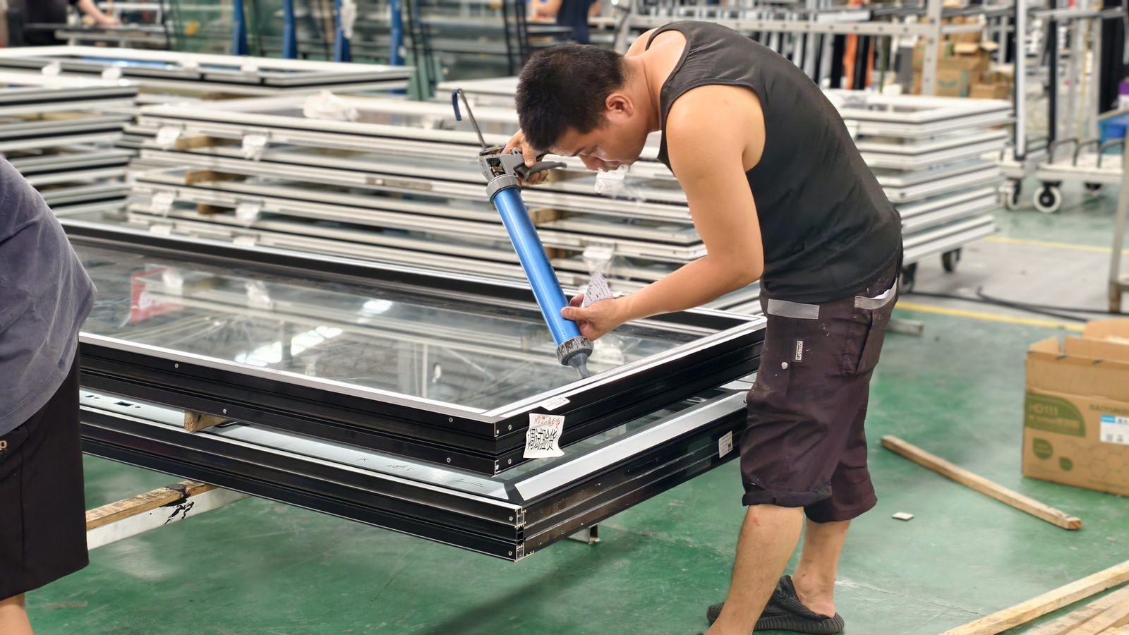 Worker applying sealant along the glass edge of an aluminium sash