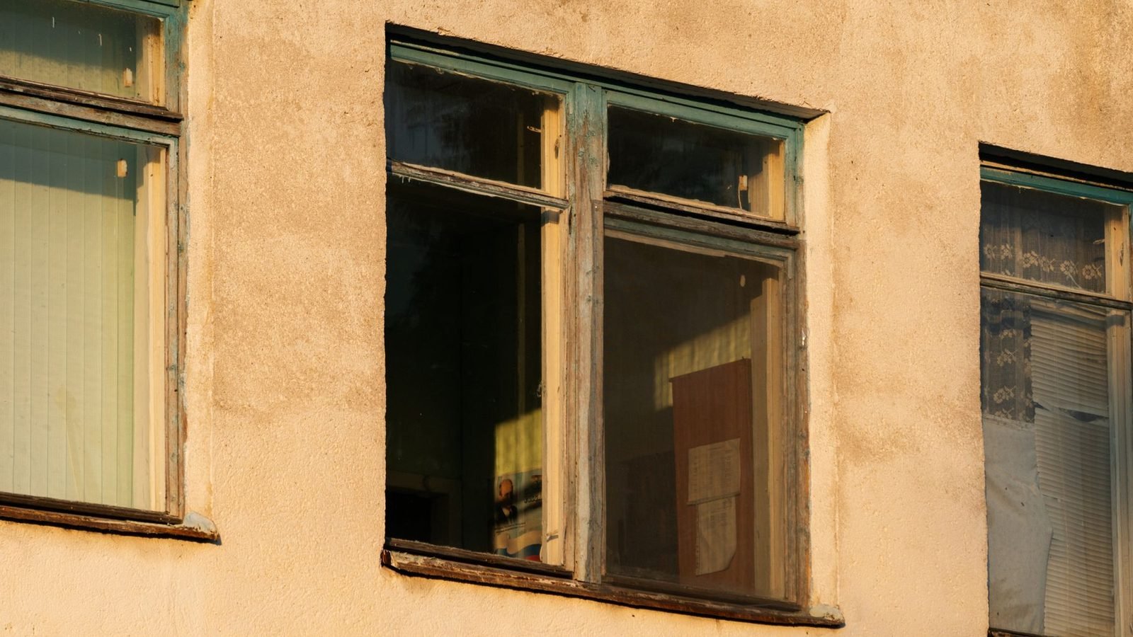 Old painted timber window frames in a rendered street facade, the openings measured one by one