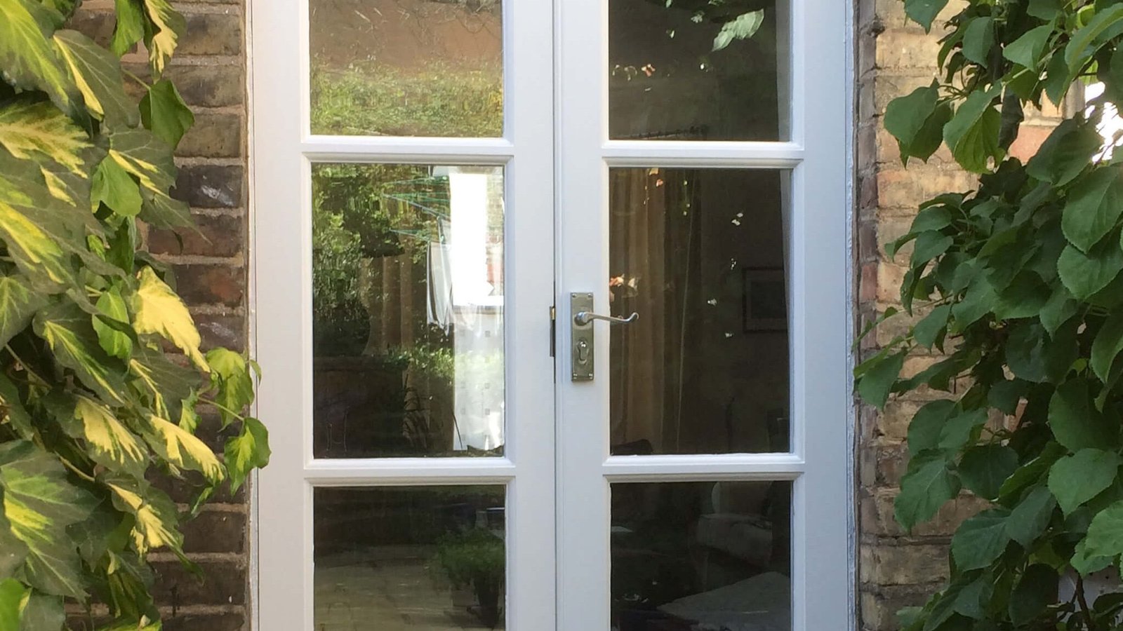 White glazed door on a brick entrance set in planted beds