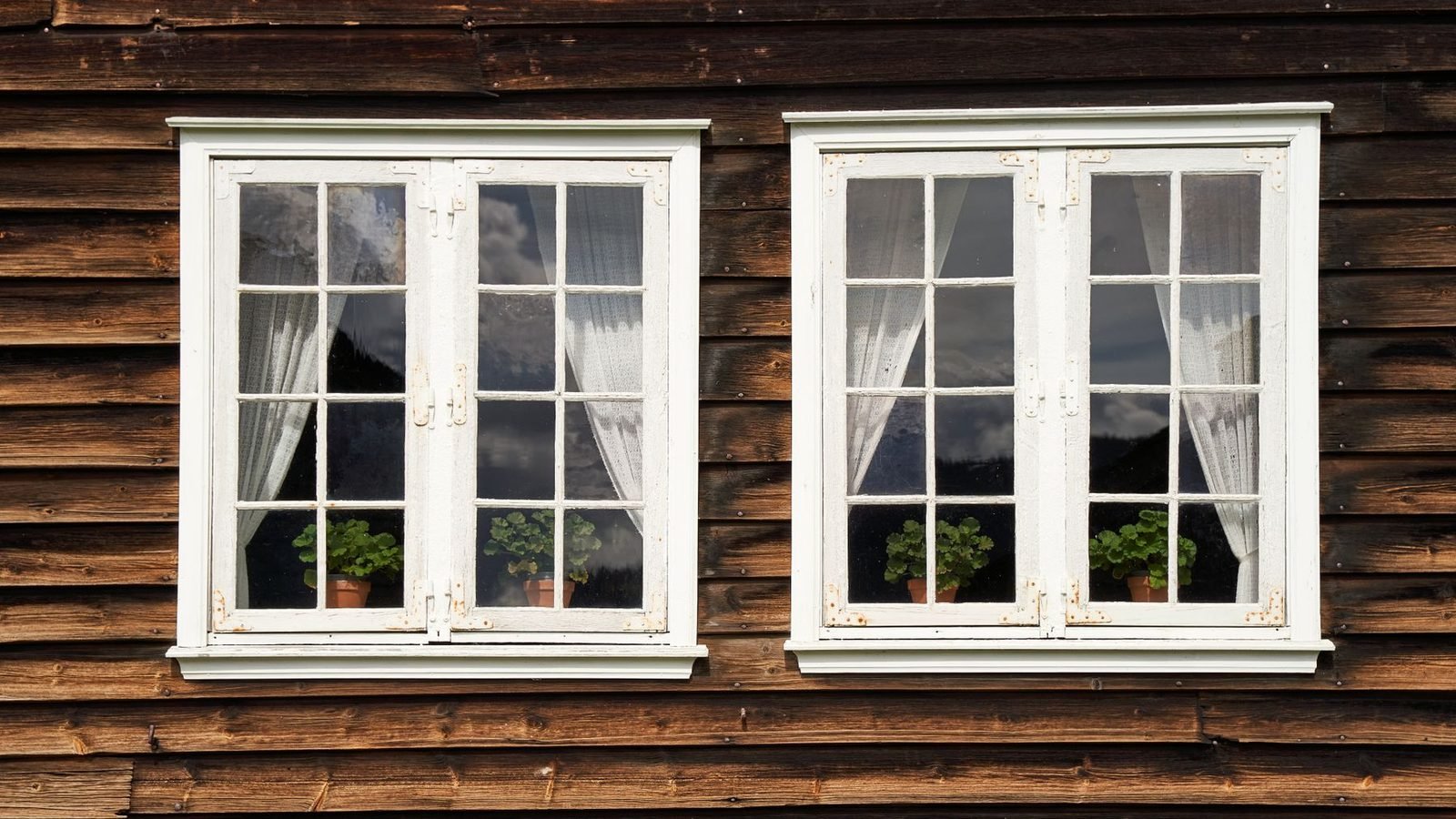 Two white casement windows set into a dark timber wall, both closed