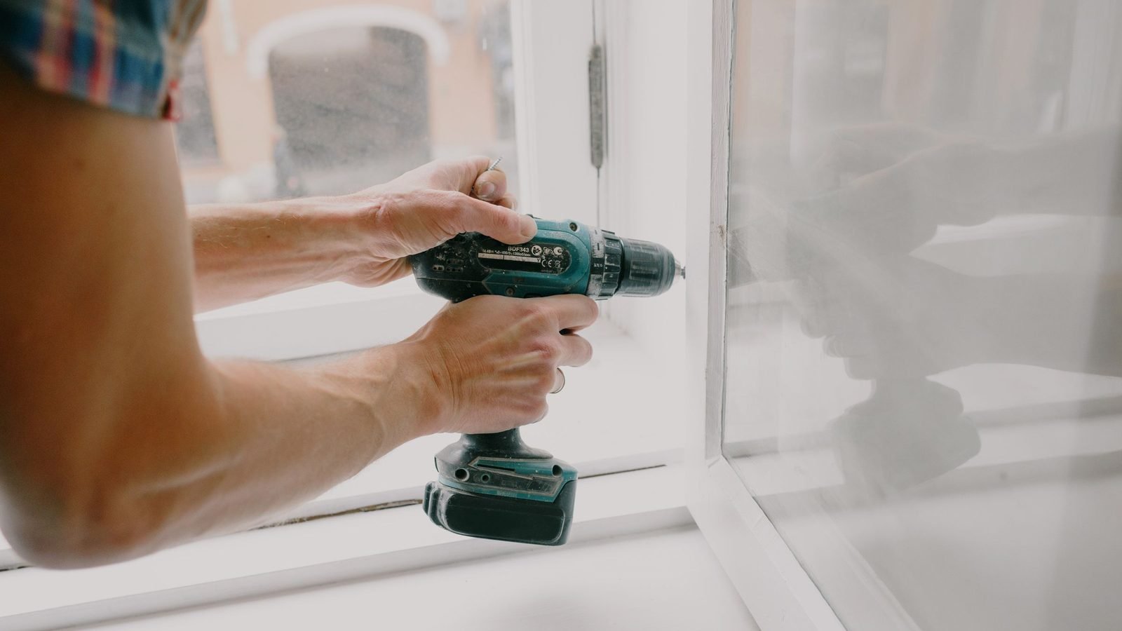 Hands driving a fixing through a window frame into the jamb of an opening
