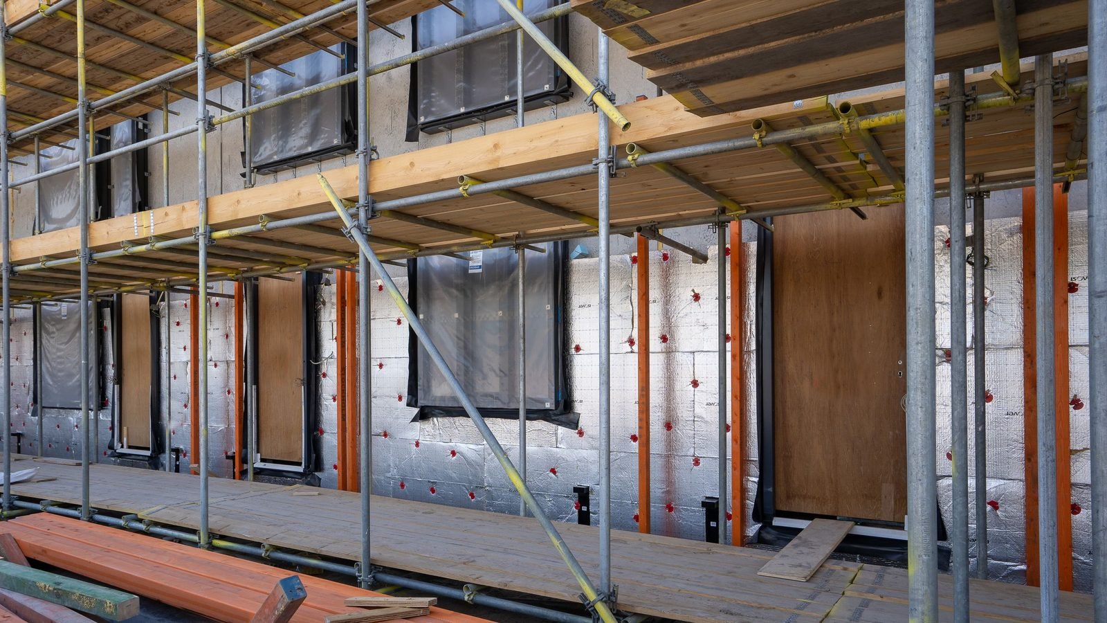 Scaffolded new-build facade with the window openings framed and the weather membrane dressed around each reveal