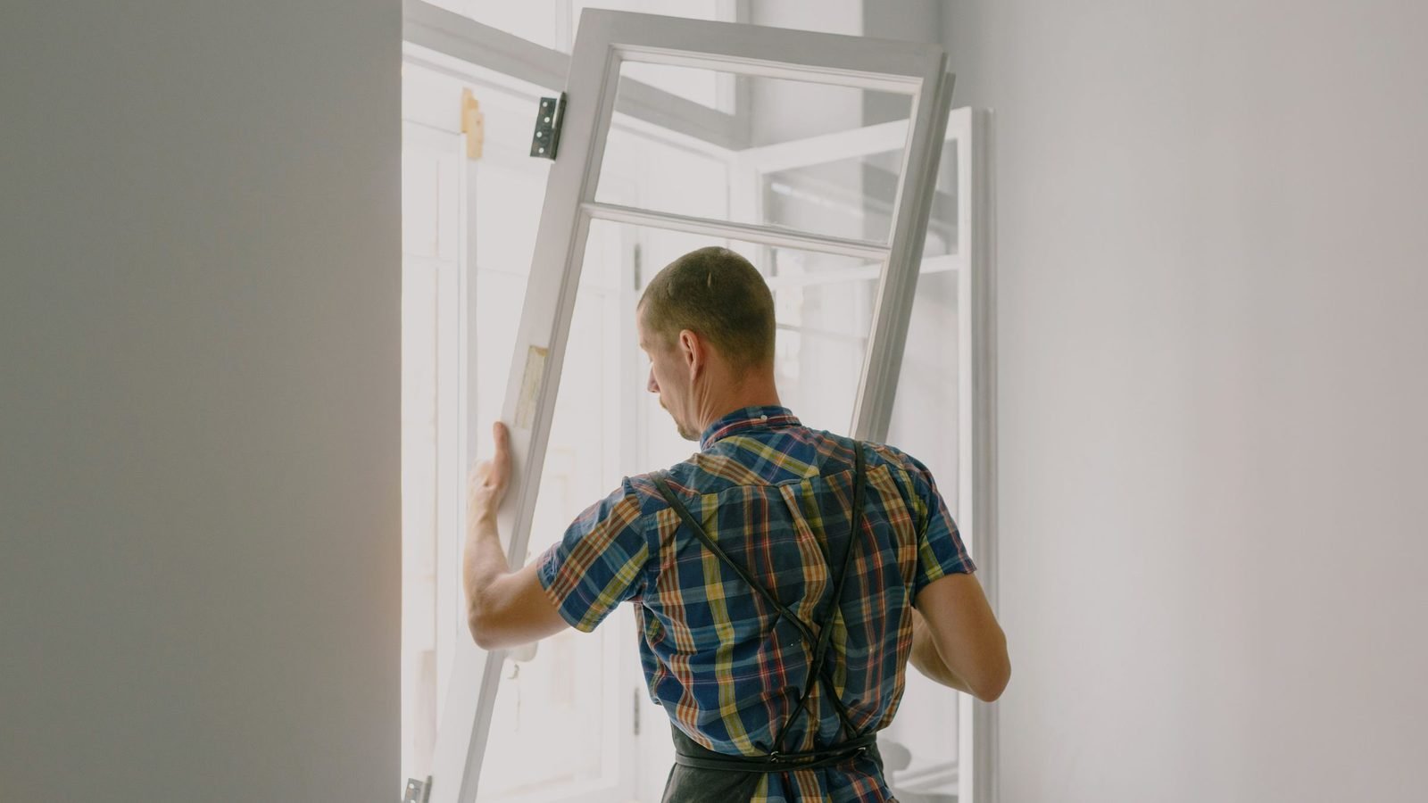 A hinged sash being lifted into its frame during installation, hinges and frame edge visible